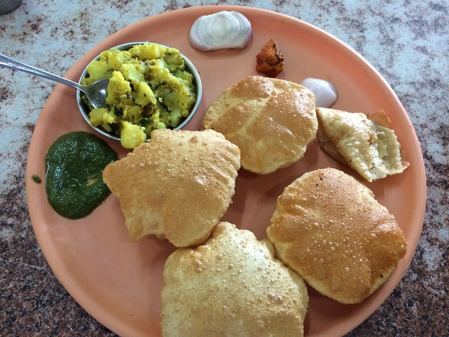 Hot bedmi poori served with spicy potato curry at a roadside stall.