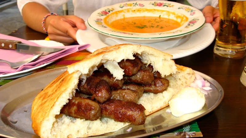 Freshly grilled ćevapi served with somun flatbread, raw onions, and a dollop of creamy kajmak.