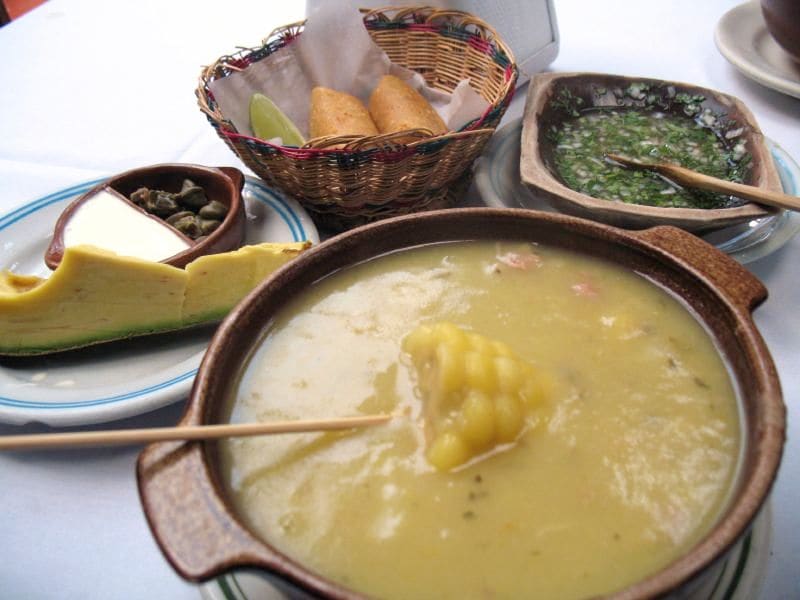 A traditional bowl of Ajiaco santafereño served with capers, cream, avocado, and rice.