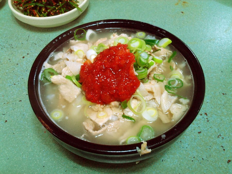 Dwaeji gukbap served with salted shrimp, chives, and steamed pork slices.