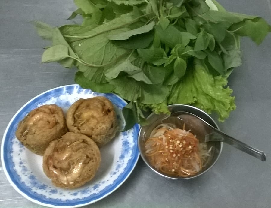 Bánh cống, fried savory cakes wrapped in leafy mustard greens and dipped in sweet fish sauce.