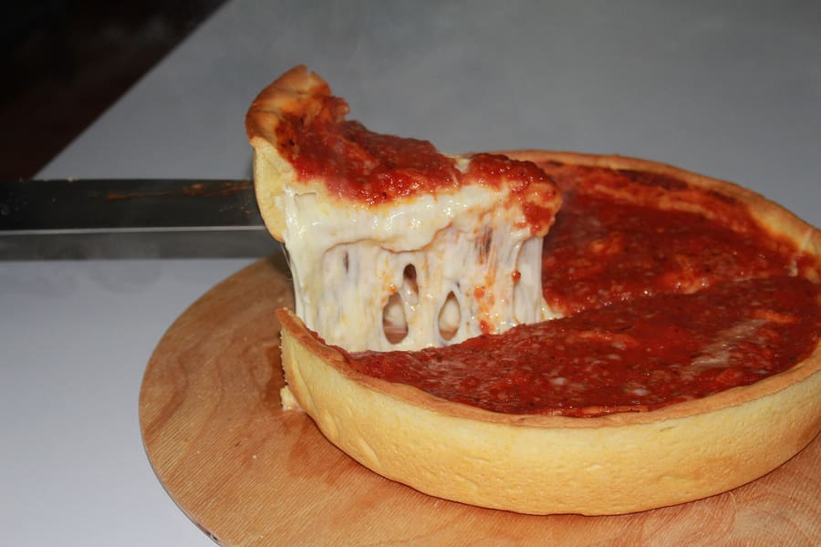 Deep-dish pizza baked in a deep steel pan with tomato sauce on top.
