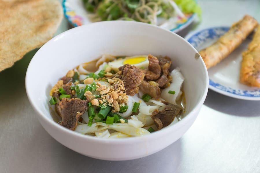 Mì Quảng served with wide turmeric rice noodles, roasted peanuts, sesame rice crackers, and pork broth.
