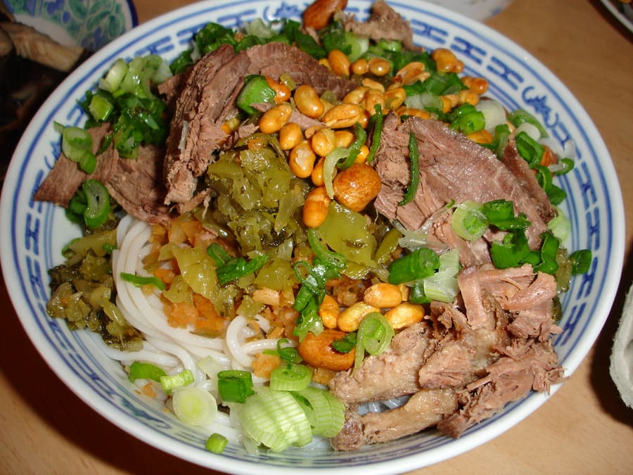 A dry bowl of Guilin rice noodles with sliced pork, gravy, and pickled chilies.