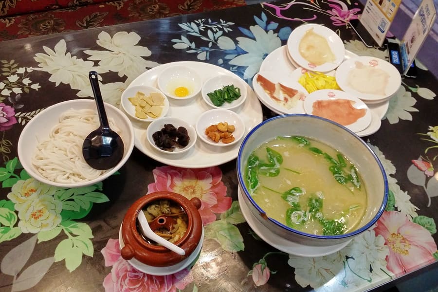 A traditional bowl of cross-bridge rice noodles served with sliced chicken, quail egg, and fresh herbs.