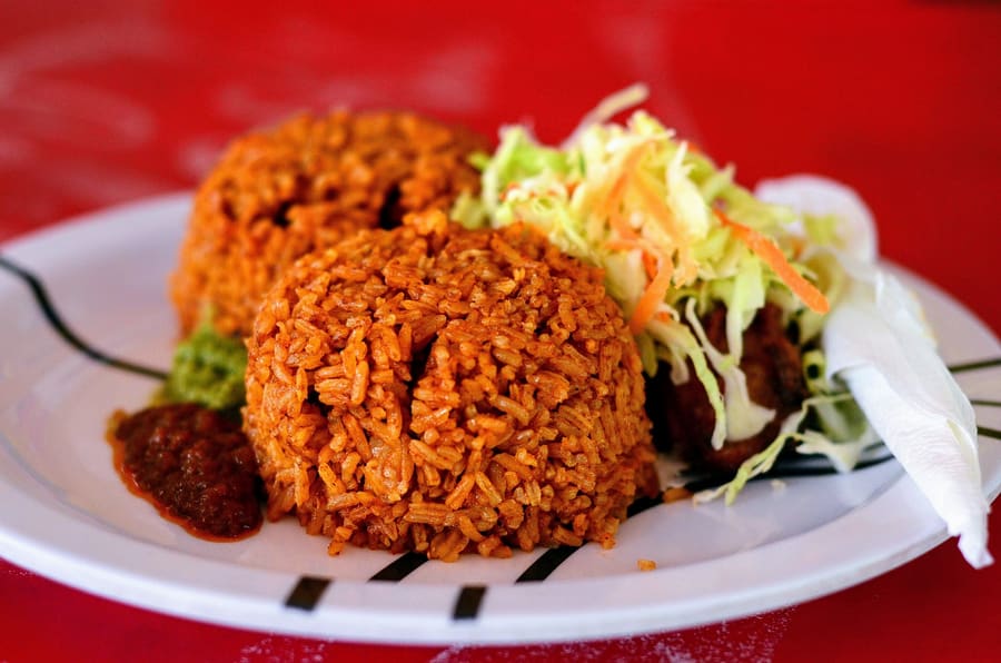 Smokey jollof rice served alongside fried plantains and grilled meat.