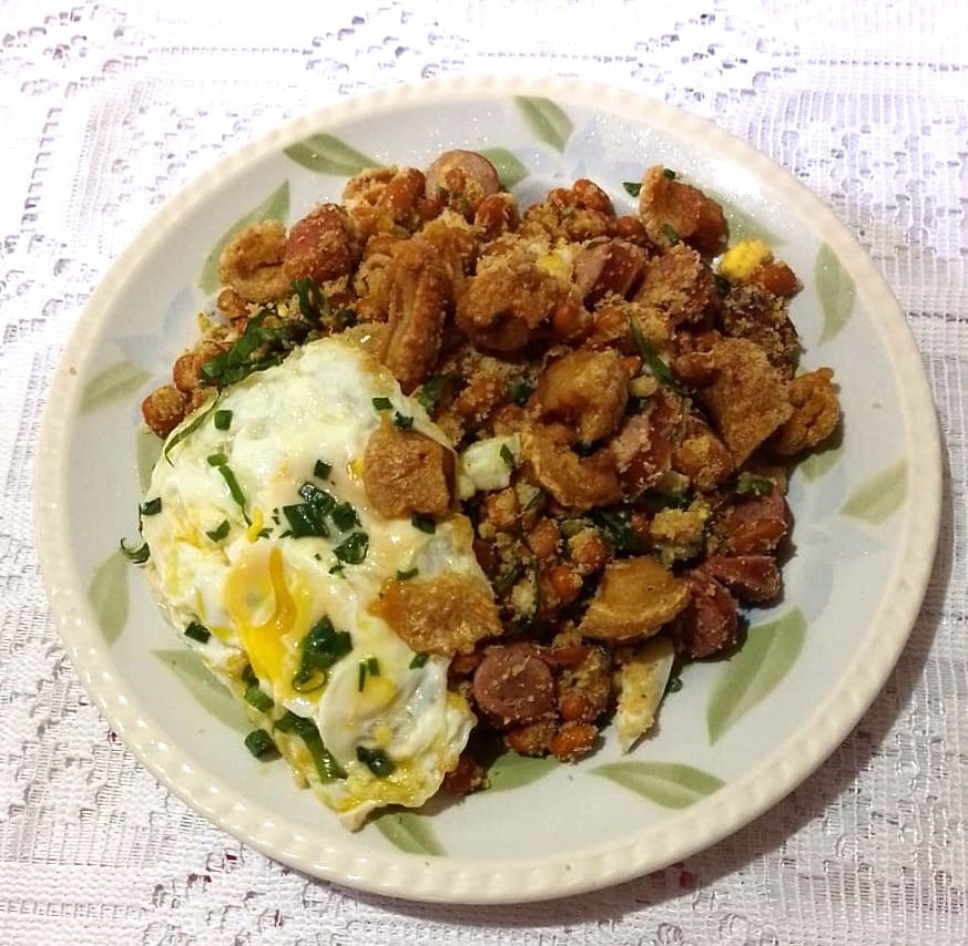 Feijão tropeiro served in a soapstone pot with pork chop and sautéed kale.