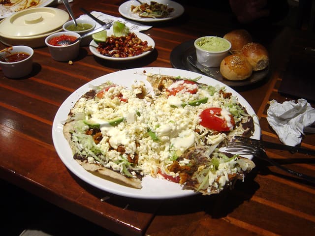 A crisp tlayuda topped with refried beans, quesillo, and grilled beef.