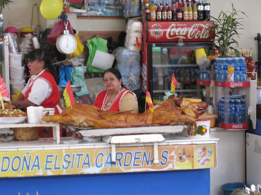 Hornado served with potato cakes (llapingachos) and toasted corn (tostado) at a local market stall.