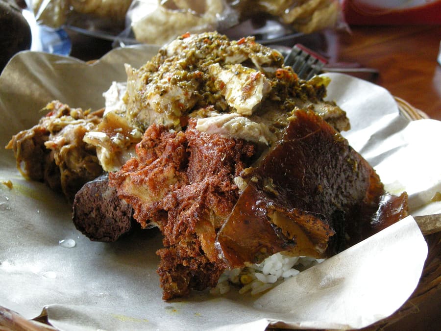 Crispy spit-roasted pork served with blood sausage and cassava leaves at local warungs.