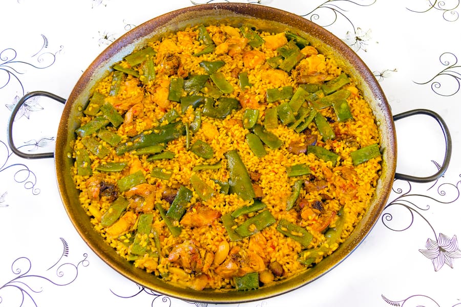 Traditional paella valenciana cooked over orange wood in flat pan.
